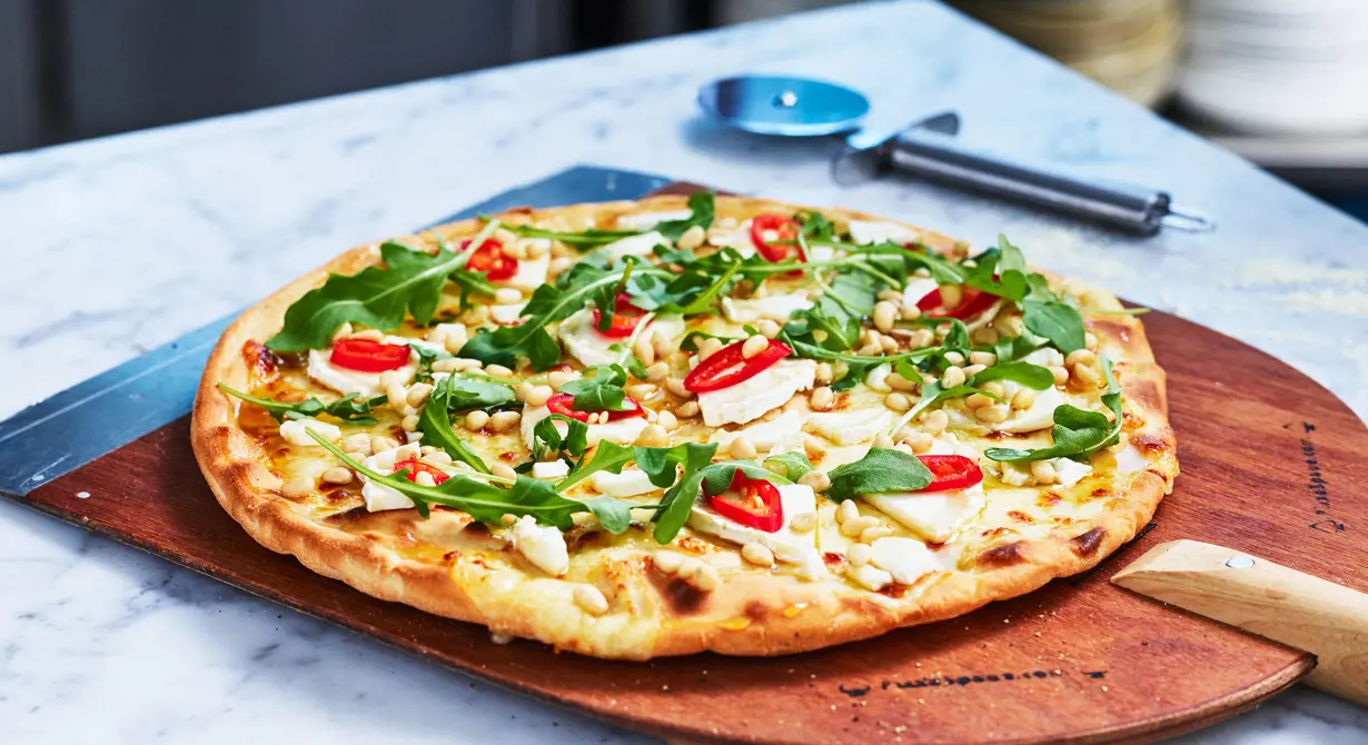 Pizza bianca med mozzarella som grund är en självklarhet på pizzamenyn idag. Ringla över honung och toppa med chèvre, chili, rucola och pinjenötter.