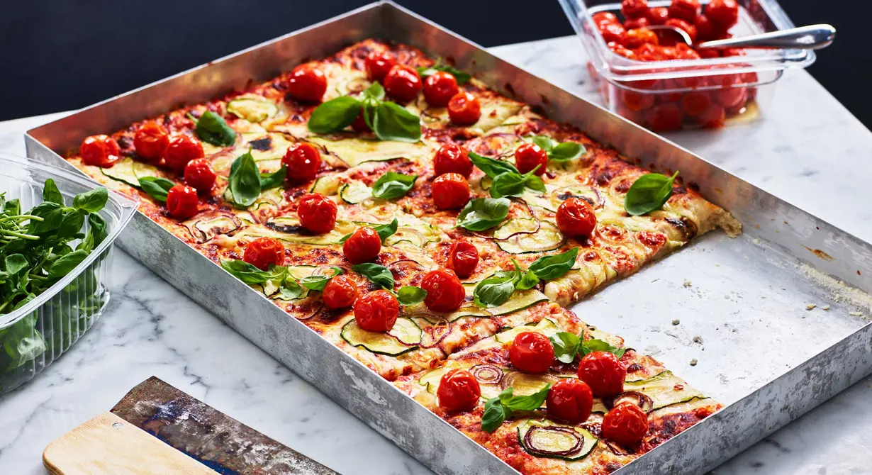 Både färskost och tomatsås är basen på den här vegetariska pizzan som bakas på färdig pizzabotten. Den toppas med tunna skivor zucchini och rödlök. Vid servering toppas pizzan med långbakade tomater och färsk basilika.