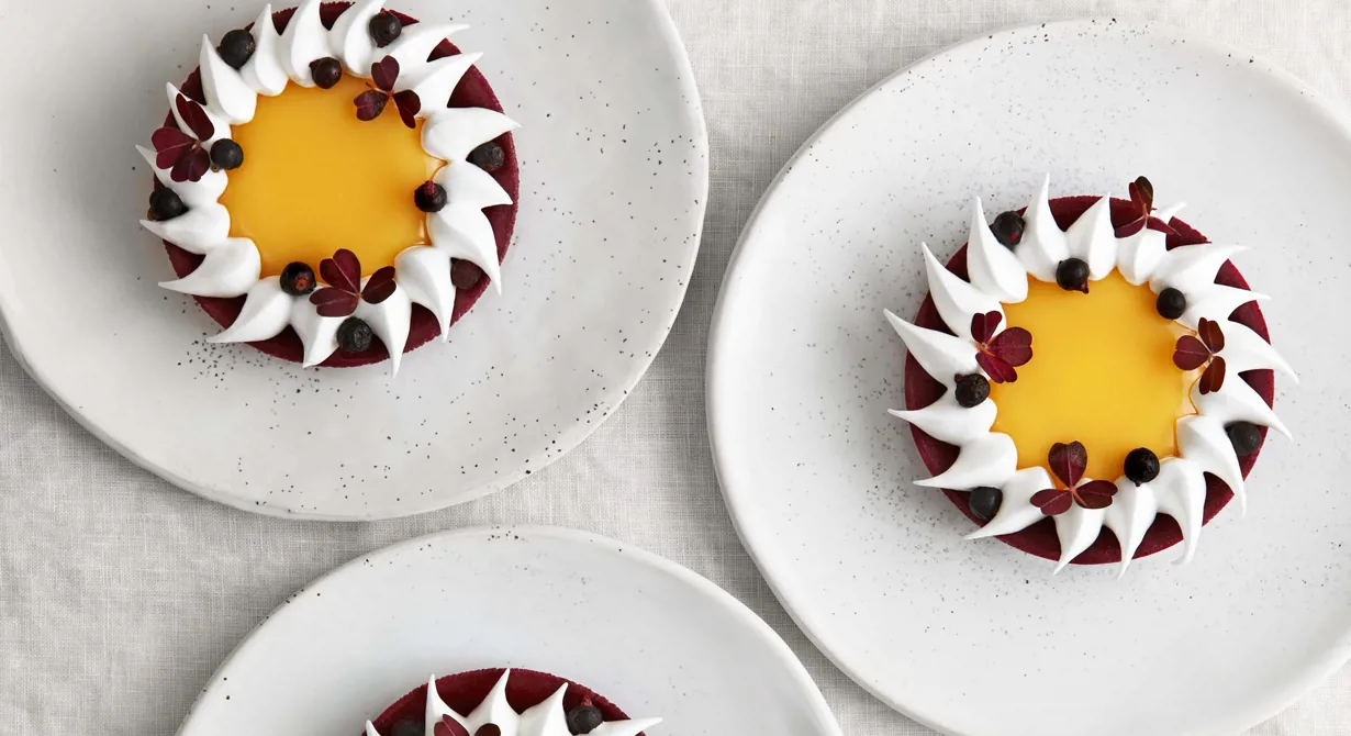 En klassiker med twist. De fina, tunna tartelettskalen fylls med en härligt syrlig curd på yuzu. Spritsade marängtoppar med smak av långpeppar och frystorkade vinbär blir som smakrika smycken ovanpå.