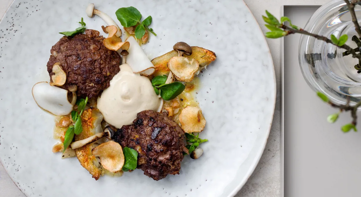En spännande rätt där biffarna på älgfärs blir saftiga av rivet äpple och serveras med syltad, friterad och rostad jordärtskocka, grillad svamp, lökvinägrett samt ett gräddigt skum på karljohan.