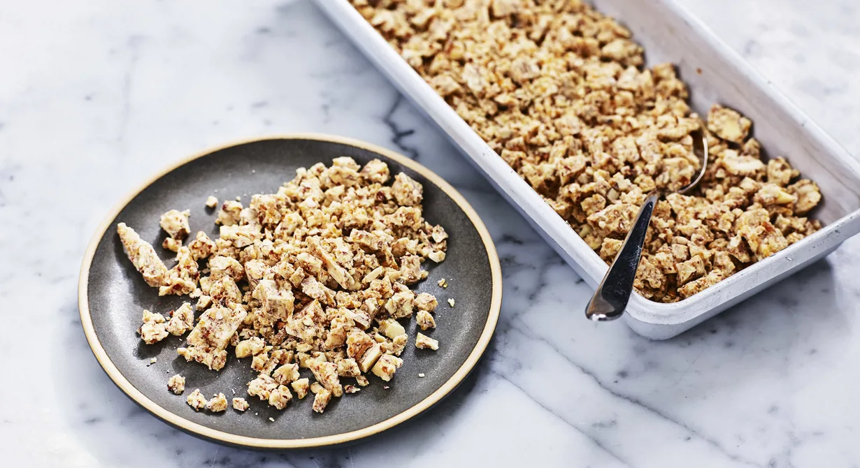 Mandeln rostas och blandas med en gyllene karamell. Den krossade mandelkaramellen blandas därefter med smält vit choklad. Efter att den stelnat kan den hackas i önskad storlek för att bli en underbar fyllning och ett härligt crunch i bakelser eller tårtor. Se t ex "Jordgubbsbakelse med brynt smör" som är framtagen av Disa Molin, Årets konditor 2018.