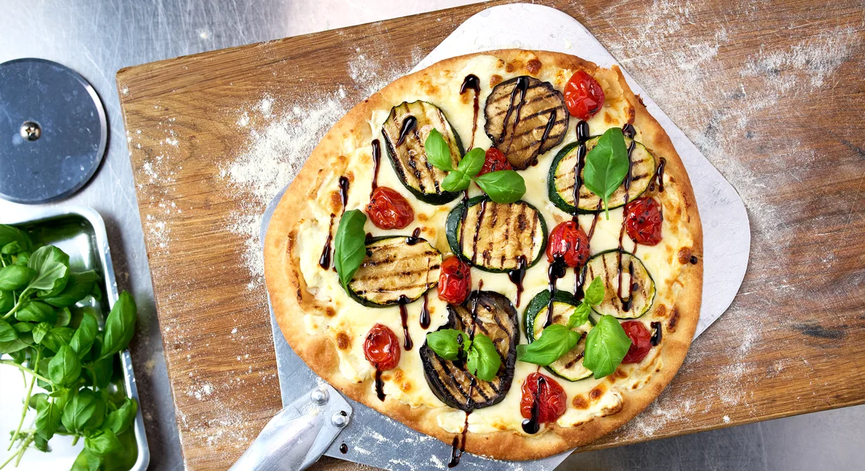 En vegetarisk pizza med krämig vitost som ger pizzan smak av fetaost. Toppa med grillad zucchini och bakade tomater. Garnera med basilika och crema di balsamico.